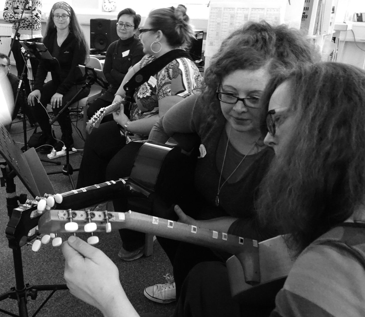A group of women playing guitars and tuning them to Figurenotes tuning A E A E