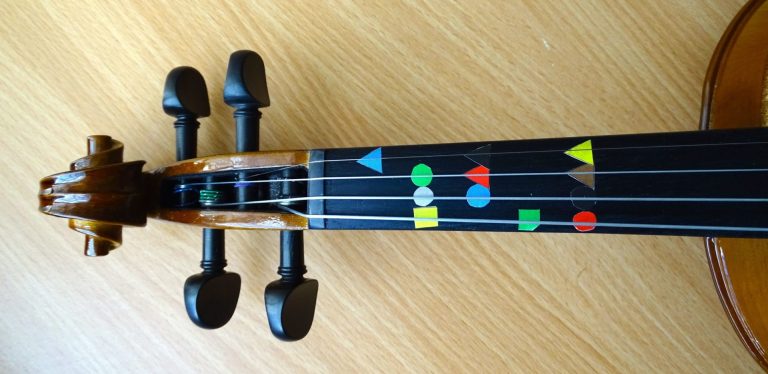 The fingerboard of a violin with Figurenotes stickers on the natural notes.