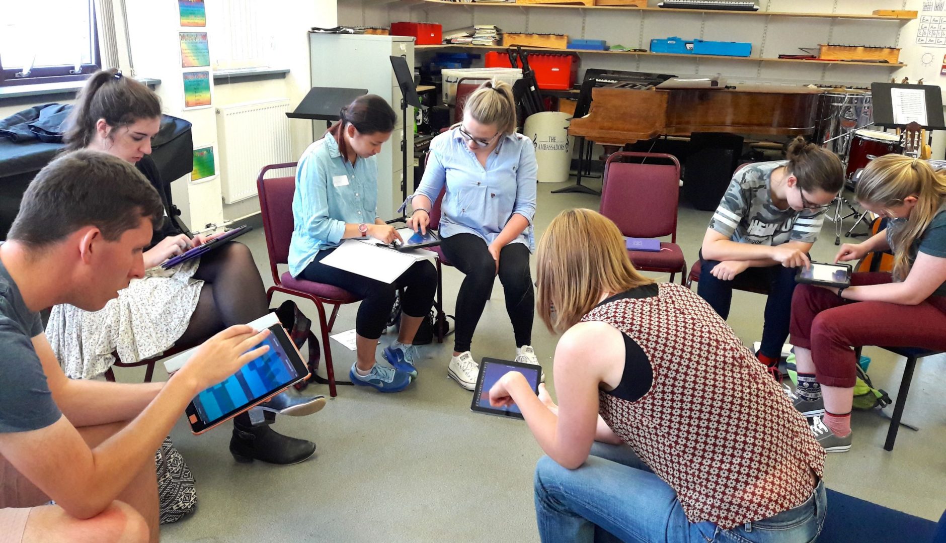 A group of students sit in a circle working on the Thumbjam apps on their iPads at a training day.