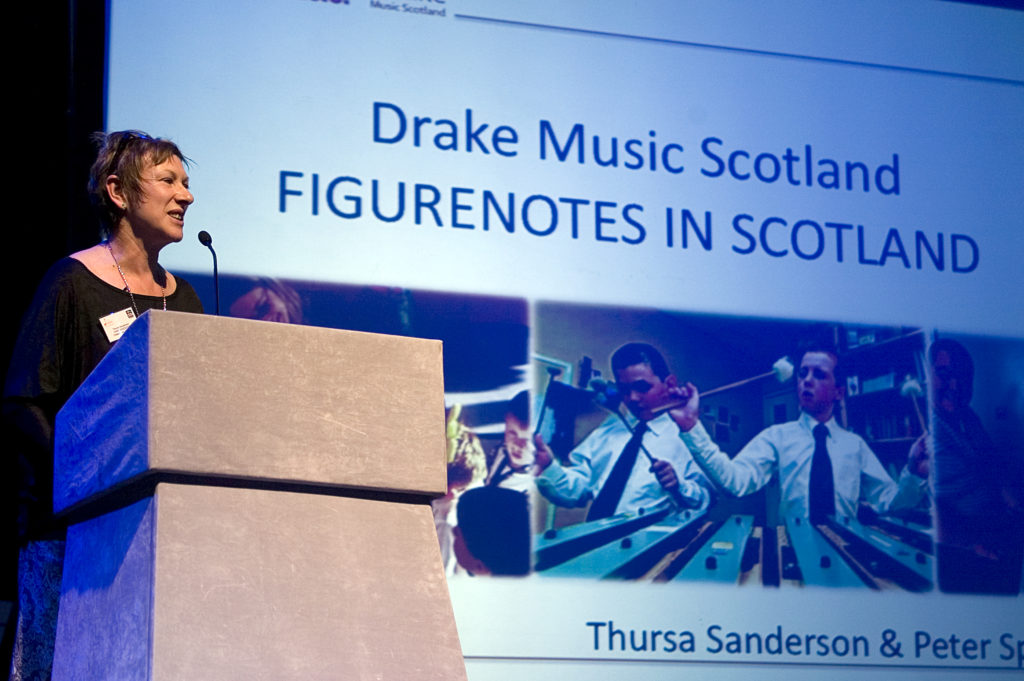 Thursa Sanderson presenting at the conference in front of screen reading 'Drake Music Scotland - Figurenotes in Scotland'