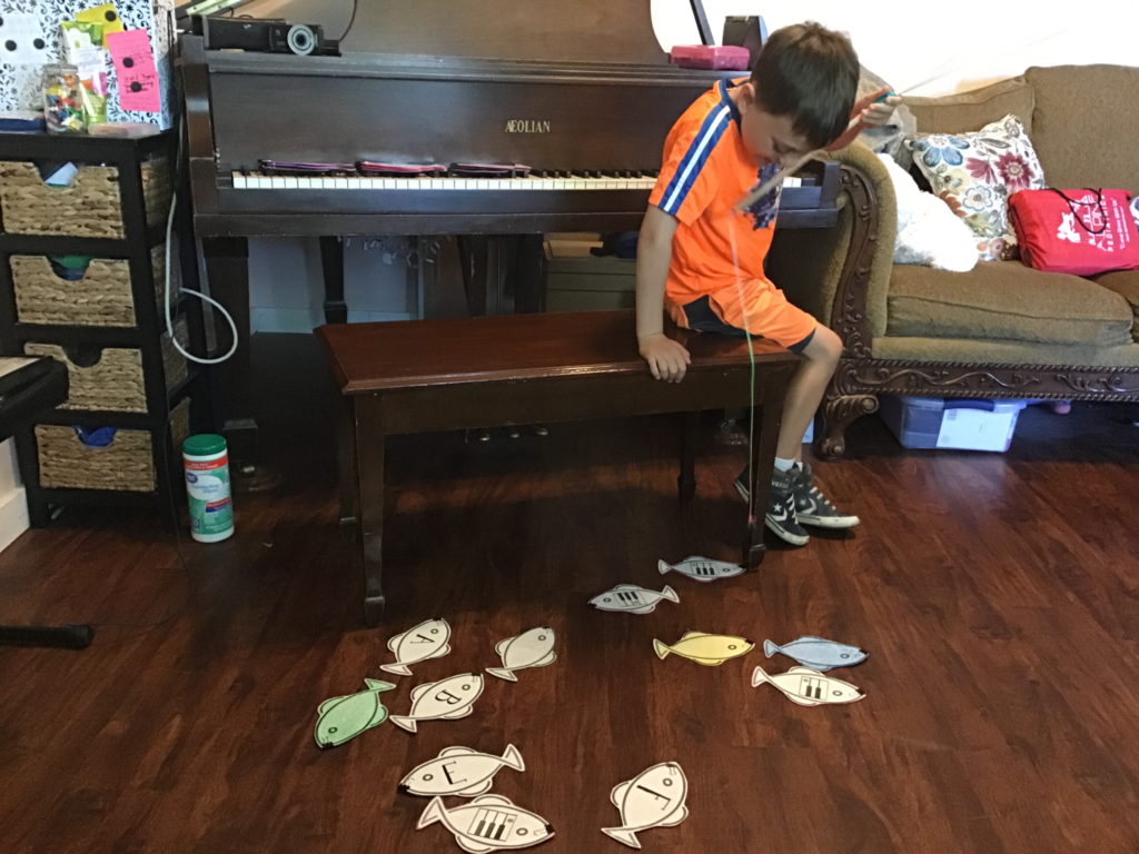 A child playing with paper fish in Figurenotes colours. The fish are spread on the floor. The child sits in front of the piano looking at the fish.