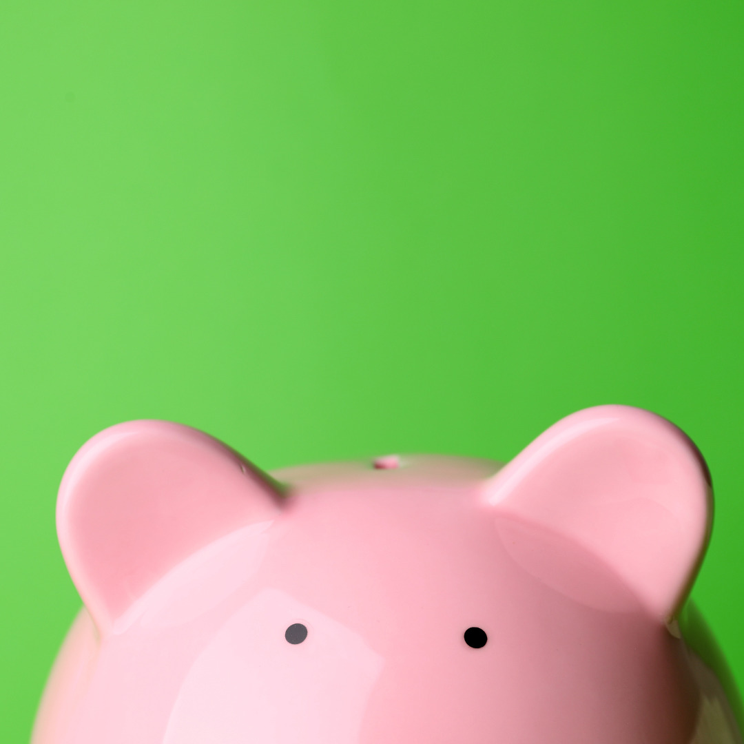 A green background with a light pink piggy bank peeking from the bottom edge. Only the area from the eyes upwards are visible.