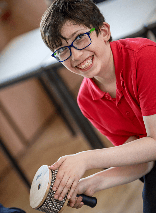 A child plays a cabasa, grinning at someone off camera.