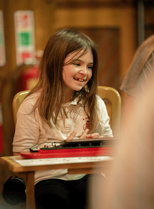 A girl with brown hair smiles softly while playing an instrument set on the table in front of her