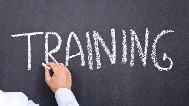 A hand writes the word 'Training' on a chalk board