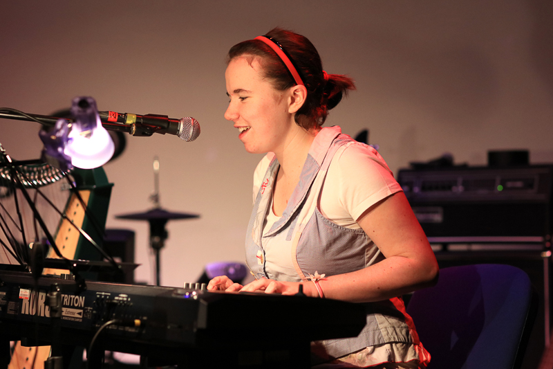 A young woman plays keyboard and sings into a microphone.