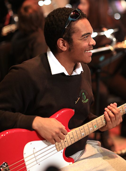 A smiling boy plays bass guitar