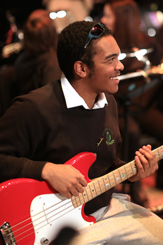 A smiling boy plays bass guitar