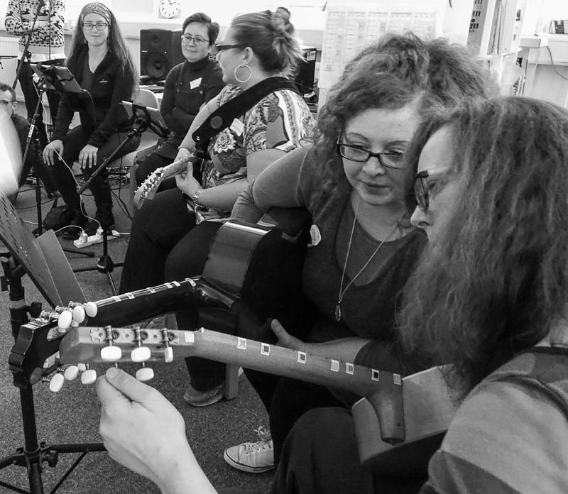 A group of people with guitars. Some are tuning and others are playing.